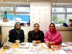 Photo shows three people from Bollyfit Active club sitting behind a desk, posing for the camera. The desk has promotional leaflets. There is a window and a pop-up banner in the background.