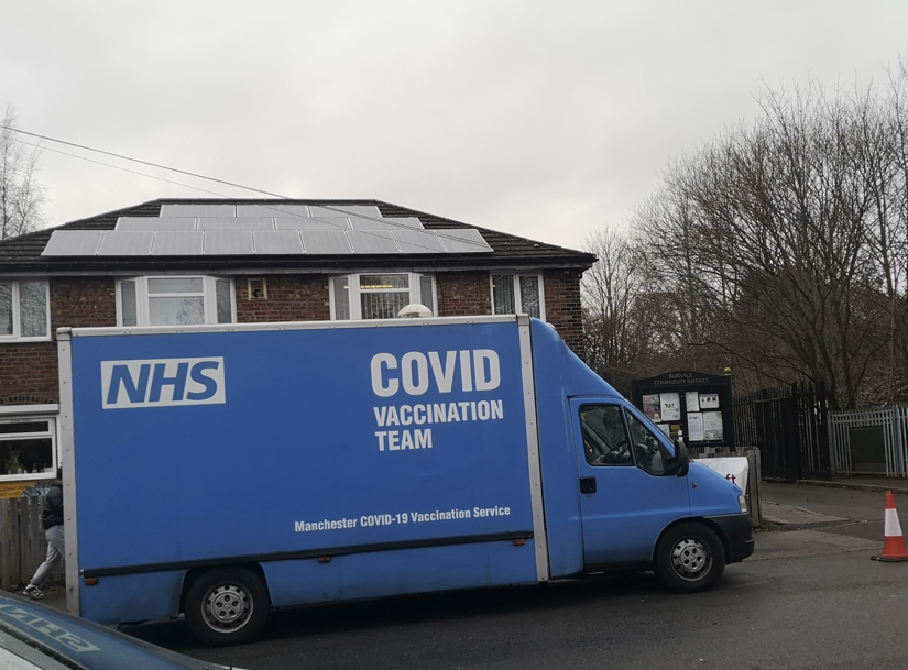Photo shows a blue NHS vaccination van. It is parked outside the Westcroft Community Centre in Burnage.