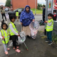 The image shows a woman and three children litter picking near Cheetham Academy Primary School