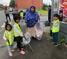 The image shows a woman and three children litter picking near Cheetham Academy Primary School