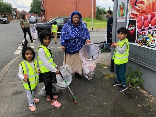 The image shows a woman and three children litter picking near Cheetham Academy Primary School